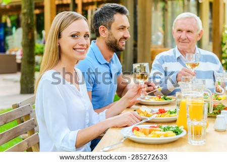 Enjoying dinner with family. Happy family enjoying meal together while woman holding wine glass and smiling