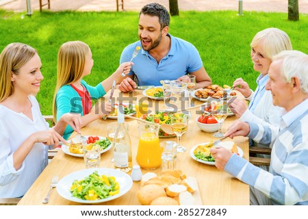 Family dining together. Top view of happy family of five people communicating and enjoying meal together while sitting at the dining table outdoors
