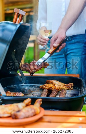Barbecuing meat on grill. Close-up of two people barbecuing meat on the grill while standing outdoors