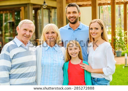Family gathering. Happy family of five people bonding to each other and smiling while standing at the back yard of their house together