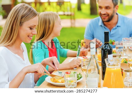 Enjoying meal together. Happy family enjoying meal together while sitting at the dining table outdoors