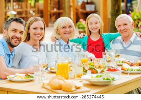 Family gathering. Happy family of five people bonding to each other and smiling while sitting at the dining table outdoors