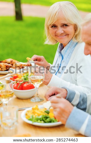 Dining with the nearest. Senior couple eating and smiling while sitting at the dining table outdoors