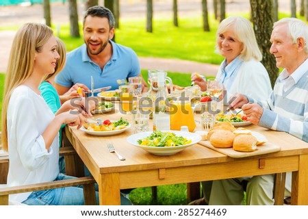 Family time. Happy family of five people communicating and enjoying meal together while sitting at the dining table outdoors