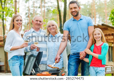 Barbeque time. Happy family of five people barbecuing meat on grill and looking at camera