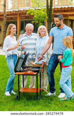 Time for barbeque. Full length of happy family barbecuing meat on grill outdoors