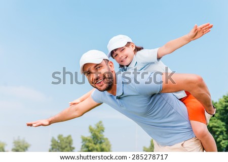 Piggyback ride. Smiling young man piggybacking his son while standing outdoors