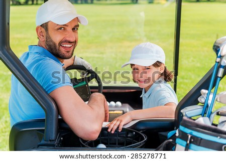 Father and son ? the best team. Cheerful young man and his son looking at camera while sitting in golf cart