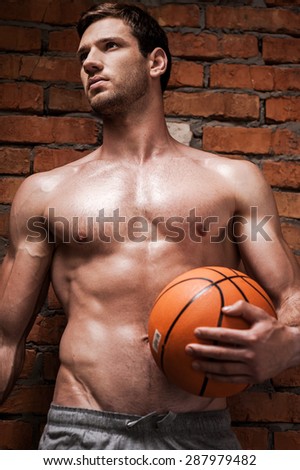 He never drops a ball. Low angle view of handsome young muscular man holding basketball ball while standing against brick wall