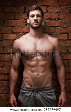 Strength and masculinity. Handsome young muscular man posing while standing against brick wall