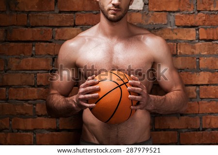 Ready to play ball. Cropped image of young muscular man holding basketball ball while standing against brick wall