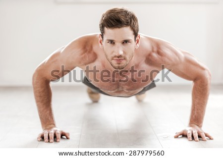 Confident man doing push-ups. Confident young muscular man doing push-ups and looking at camera