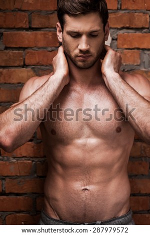 My body is a reflection of my lifestyle. Handsome young shirtless man holding hands behind neck and keeping eyes closed while standing against brick wall