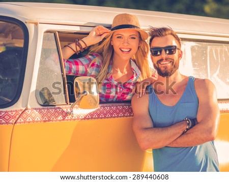 Life is better when we are together! Joyful young woman sitting inside of retro minivan and looking through the vehicle window while man standing outside and smiling