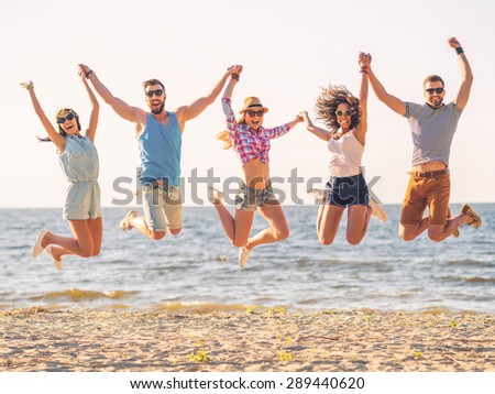 Summer fun. Group of happy young people holding hands and jumping with sea in the background