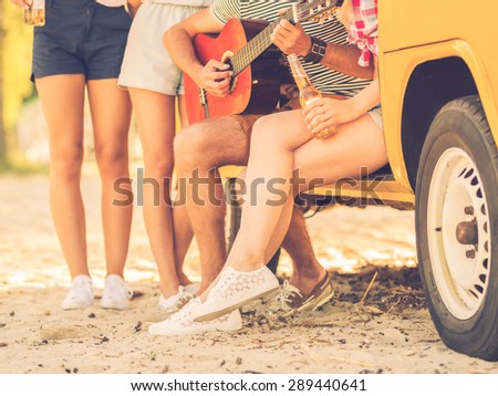 Happy time with friends. Close-up of group of young people spending time together near their minivan while one man playing guitar