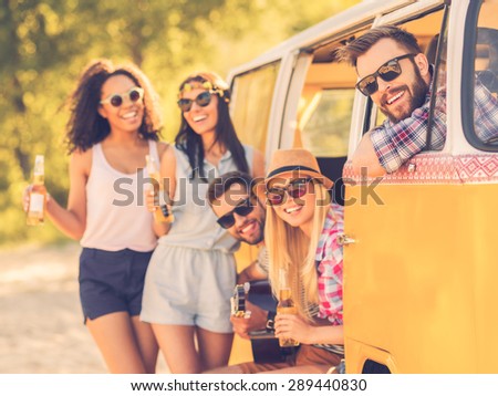 Life is brighter when friends are near. Group of cheerful young people enjoying time together while sitting and standing near their retro minivan