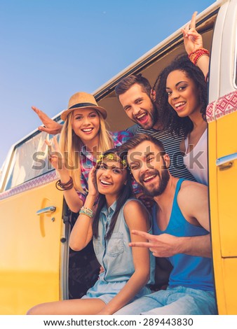 Our lives are full and happy. Group of happy young people smiling at camera and gesturing while sitting inside of retro mini van