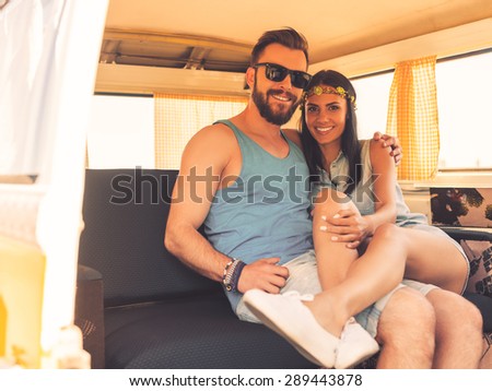 Hippie love. Happy young couple bonding to each other and smiling while sitting at the back seats of their minivan