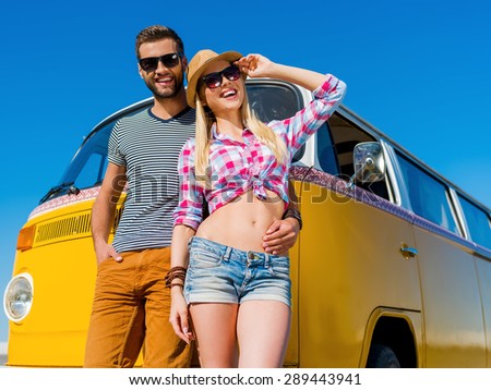 The perfect summer date. Cheerful young man embracing his girlfriend while both leaning at their retro mini van