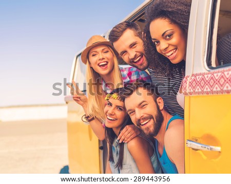 Fun time with friends. Group of happy young people smiling at camera while sitting inside of retro mini van