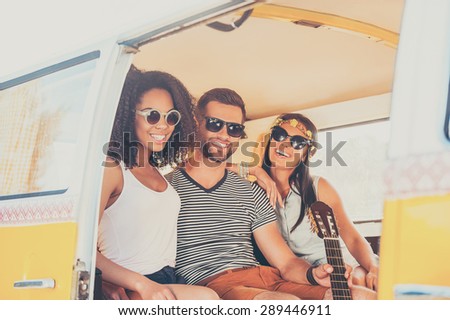 Enjoying summer with friends. Two young women and man bonding to each other and smiling while sitting together inside of the retro van