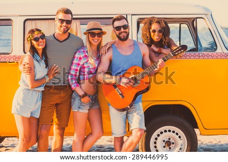 Friends forever. Group of young cheerful people standing near their retro minivan and smiling