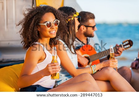 Moments of happiness. Happy young African woman holding beer and smiling while sitting together with her friends on the beach