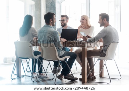 Working on new project together. Group of confident business people in smart casual wear working together while sitting at the desk in office