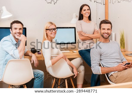 Confident business team. Group of cheerful business people in smart casual wear sitting at the desk together and smiling