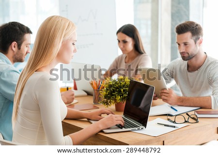 Working at new project together. Group of confident business people in smart casual wear working together while sitting at the desk in office