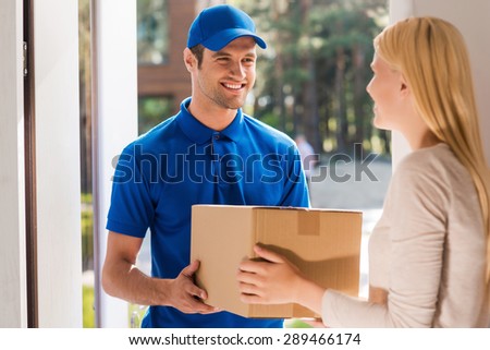 Fast and reliable service. Cheerful young delivery man giving a cardboard box to young woman while standing at the entrance of her apartment