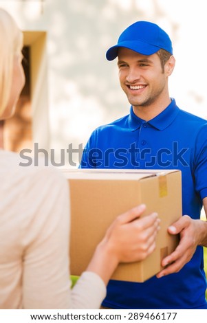 Delivering each package with smile. Happy young courier giving a cardboard box to young woman while standing outdoors
