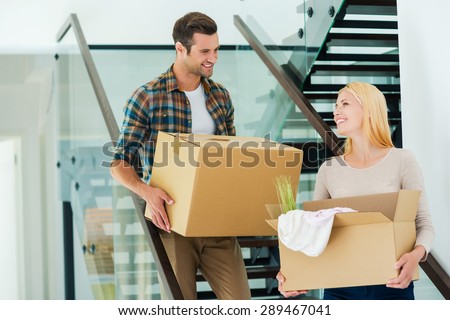 Happy to do everything together. Happy young couple holding cardboard boxes while going down the stairs
