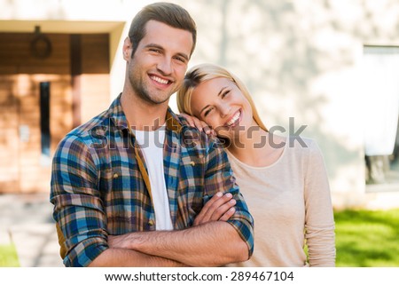 Happy young couple. Happy young couple bonding to each other and smiling while standing against their new house