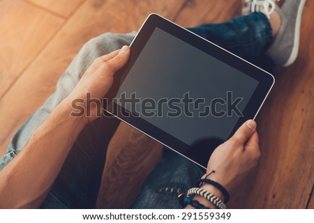 All the world in my hands. Close-up top view of man holding digital tablet while sitting on the wooden floor