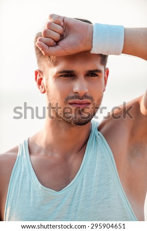 It was intense training. Pensive young muscular man holding hand near his forehead and looking away while standing outdoors
