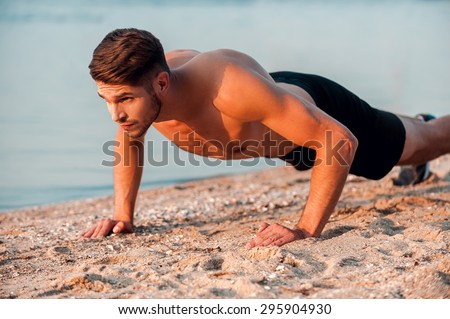 Man doing push-ups. Handsome young muscular man doing push-ups at the riverbank