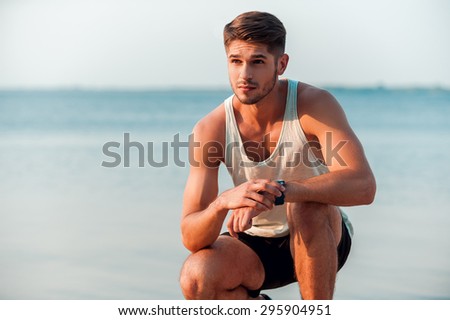 Ready to beat his time. Thoughtful young muscular man checking time on his watches while sitting outdoors