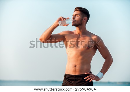 Taking a break for drinking. Confident young muscular man drinking water and holding hand on hip while standing outdoors