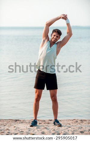 Getting his fitness on. Smiling young muscular man training while standing on the riverbank