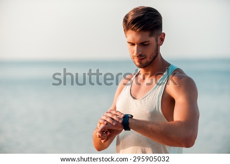 Ready to match his time. Confident young muscular man checking time on his watches while standing outdoors