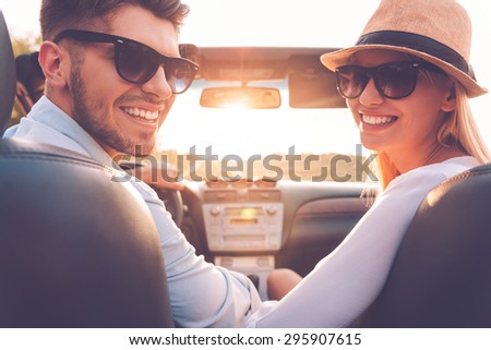Our perfect weekend journey. Rear view of cheerful young couple looking over shoulder and smiling while sitting inside of their convertible