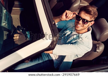 I love this car! Top view of handsome young man looking at camera and adjusting eyewear while driving his white convertible