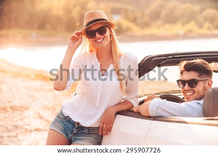 Leisure time we are spending together. Happy young woman leaning at white convertible while her boyfriend sitting on the front seat of it