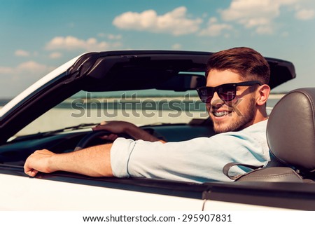Keep on driving. Rear view of happy young man looking over shoulder and smiling while driving his white convertible