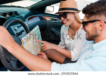 I think we should turn here. Happy young couple examining the map while sitting in their convertible