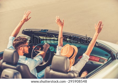 Getting away from it all. Top view of cheerful young couple keeping arms raised while riding in their white convertible