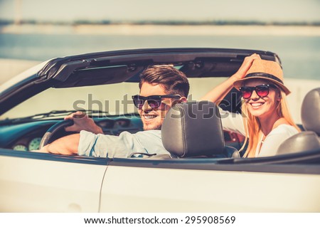 Getting away on weekend. Cheerful young couple smiling at camera while riding in their white convertible
