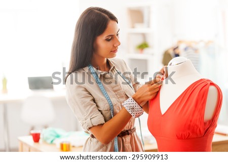 Perfecting the style. Beautifulyoung woman pinning textile on dress while standing in her fashion workshop